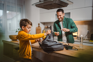 Dad prepare chocolate cream on bread while son pack backpack school
