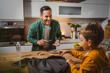 Dad prepare chocolate cream on bread while son pack backpack school