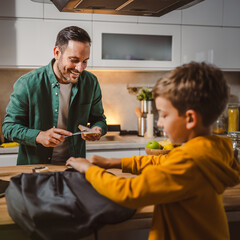 Dad prepare chocolate cream on bread while son pack backpack school