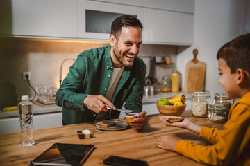 Dad prepare chocolate cream on bread while son pack backpack school
