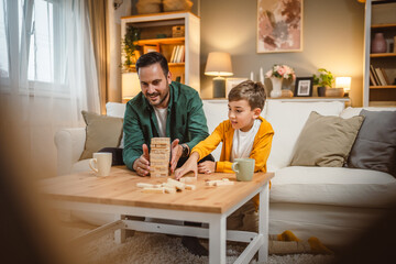 Father with cup of hot drink and son play board game together at home