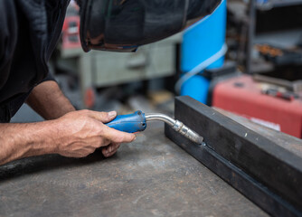 Carrying out a weld: the man with the welding mask positions himself with the welding machine on the welding point. Conceptual image of work, metalworking, craftsmanship. Copyspace.