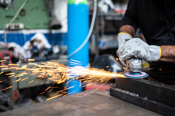 Using the flexible disc grinder on a metal bar: When the tool touches the surface, numerous orange sparks are projected. Concept of metal processing in the workshop. Craft work, metal working.