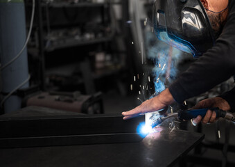 Spectacular conceptual image of a blacksmith busy using the welding machine. Sparks and smoke flash from the tip of the soldering iron. Blurred background. Welding, repair, work concept. Copy space.
