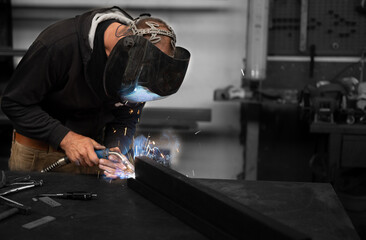 Spectacular conceptual image of a blacksmith busy using the welding machine. Sparks and smoke flash from the tip of the soldering iron. Blurred background. Welding, repair, work concept. Copy space.