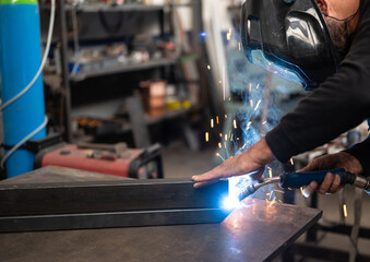 Spectacular conceptual image of a blacksmith busy using the welding machine. Sparks and smoke flash from the tip of the soldering iron. Blurred background. Welding, repair, work concept. Copy space.