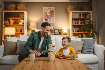 Father with cup of hot drink and son play board game together at home