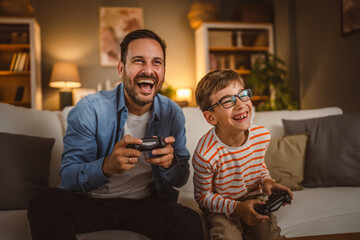 Adult caucasian father and son play video games with joystick at home