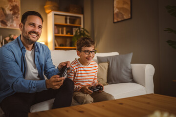 Adult caucasian father and son play video games with joystick at home