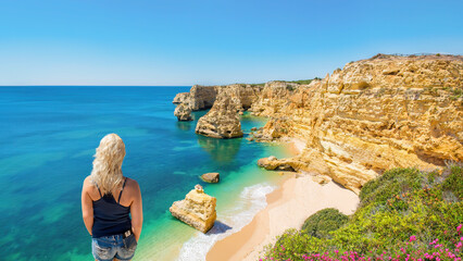 A blonde haired woman looks at  the beach and coastline at Praia da Marinha, Algarve, Portugal.