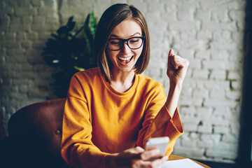 Emotional female in eyewear happy from getting good job offer via mail on digital cellular.Joyful...