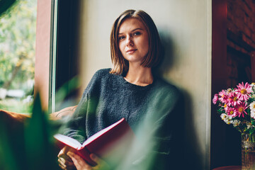 Half length portrait of attractive female reader with short haircut looking at camera spending...