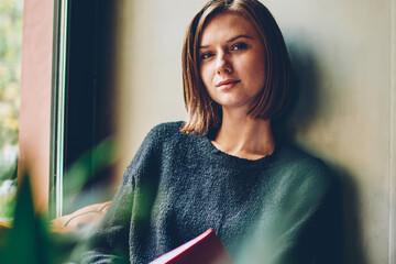 Half length portrait of attractive female reader with short haircut looking at camera spending...