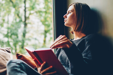 Thoughtful young woman looking out of window pondering on idea and plot of new bestseller of...