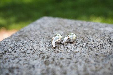 Composition of a pair of silver earrings on a large, raw granite stone. The earrings are teardrop-shaped