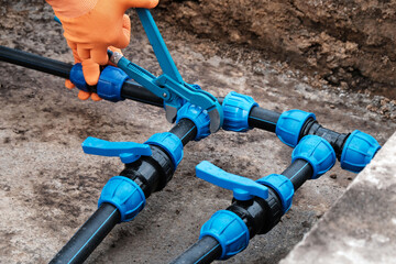 Plumber using a wrench tightens a compression fitting onto a HDPE pipe with a tap, installing a...