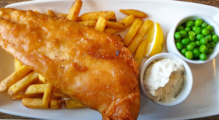 Top down view of classic English meal of fish and chips with peas and tartar sauce