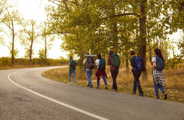 Obraz premium Group of friends tourists trekking with backpacks walking in the forest. People men and women on a hiking trip holiday in nature standing in a row. Adventure, travel and tourism concept.