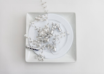 Silver curled ribbon on a square and round white plate on a white background