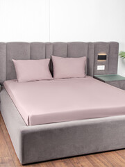 Pink bedsheet with an elastic band on bed. Bedsheet and two pillows