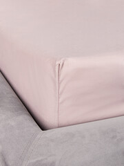 Bedsheet with an elastic band. Corner closeup. Pink bed linen on gray bed