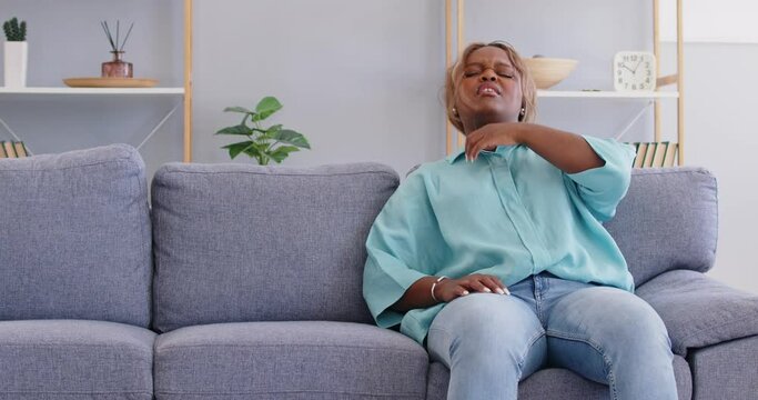 Sick african american woman sitting alone on sofa in living room at home feeling unhealthy and losing consciousness. Young girl having heart attack and fainting. Healthcare concept. 4k video.