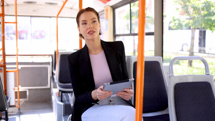 Beautiful, young businesswoman riding in a city bus and using a digital tablet