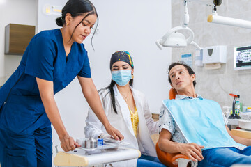 A dental assistant is passing dental treatment instruments to the professional in a private dental...