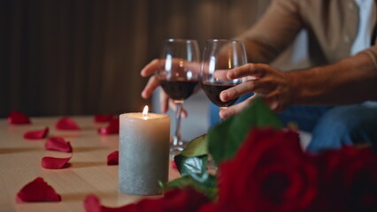 Loving boyfriend taking wine glasses from table with lying red roses close up. 