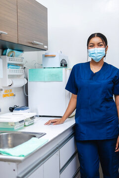 Dental assistant in the disinfection and sterilization area, looking at the camera with a positive attitude. She is wearing an anti-fluid uniform and a face mask. The place looks aesthetic and clean