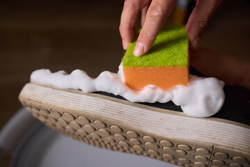 A person is scrubbing a shoe with a sponge and foamy cleaner