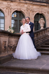 Fototapeta premium Beautiful couple, newlyweds on a walk. Bride and groom are standing on steps of the palace. Family