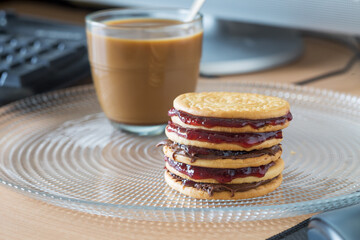Cookies with chocolate and strawberry jam on glass plate and coffee with milk in the background.