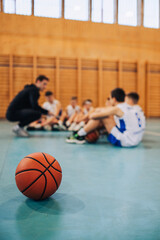 Naklejka premium A basketball at indoor court with junior basketball team in background