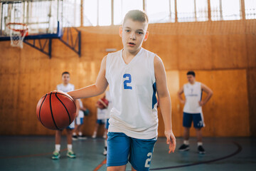 A young athlete dribbling a basketball on training at indoor court.