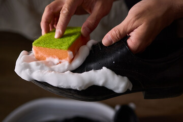 A person is scrubbing a shoe with a sponge and foamy cleaner