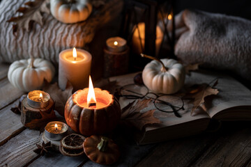 Autumn composition with burning candles, mini munchkin pumpkins, warm wool knitted sweater on the...