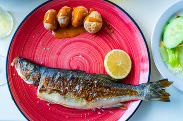Full sea bass dorado fish served on a plate with baked potatoes and slice of lemon, Mediterranean diet