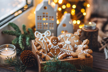 Handmade zero waste gift for Christmas or New Year. Wooden box with homemade delicious gingerbread cookies decorated with white icing. Cozy home atmosphere, fairy lights, fir tree branches