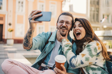 Close up of smiling silly hipster couple taking selfies on street.