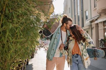 Affectionate alternative couple with skateboards kissing on city street