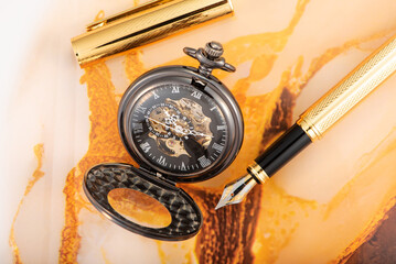 Beautiful pocket watch and vintage fountain pen on rustic wood, selective focus.