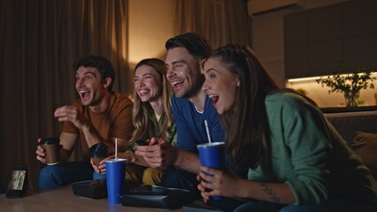 Joyful buddies enjoy tv show with drinks snacks at home evening close up. 