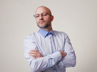 Portrait of a bald man with grey beard wearing light blue shirt, light color background. Middle...