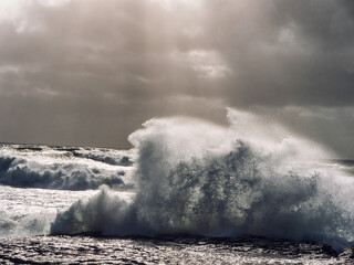 A large wave crashing onto the shore, with the water spraying high into the air. Scene is powerful...