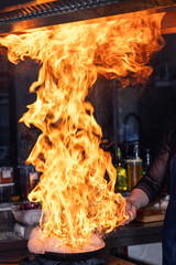 Chef creates flame in pan. Chef cooking with flame in a frying pan on a kitchen stove. Young chef...