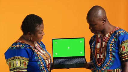 Ethnic people pointing to laptop with greenscreen layout, posing on camera with wireless pc showing...