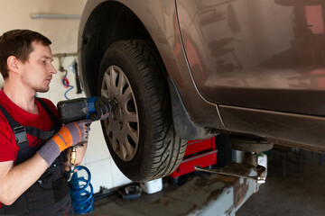 a mechanic stands by a car in a car service center. master removes a wheel from a car, repair,...