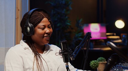 African american woman doing podcast in apartment studio, wearing headphones and talking on...