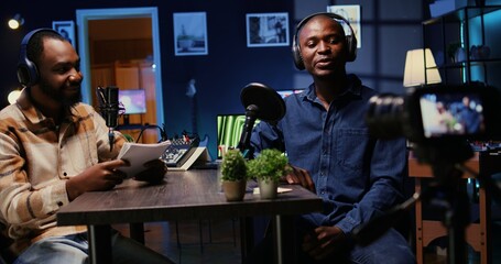 African american host engaging in entertaining discussion with man during livestream in apartment studio, making him laugh. Presenter uses high tech filming gear to produce comedy podcast
